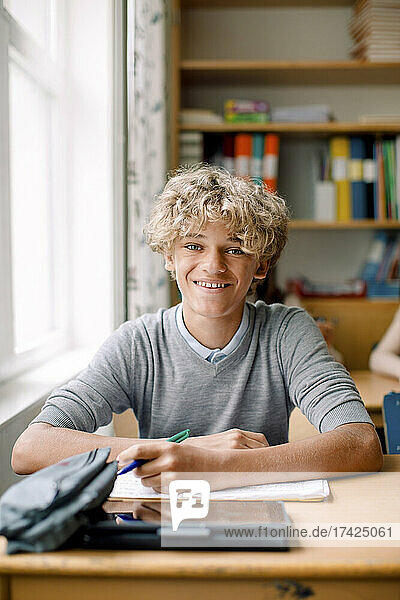 Smiling blond teenage boy at desk in classroom