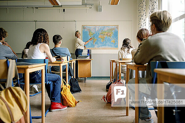 Lehrerin unterrichtet Mädchen und Jungen im Klassenzimmer über Landkarten