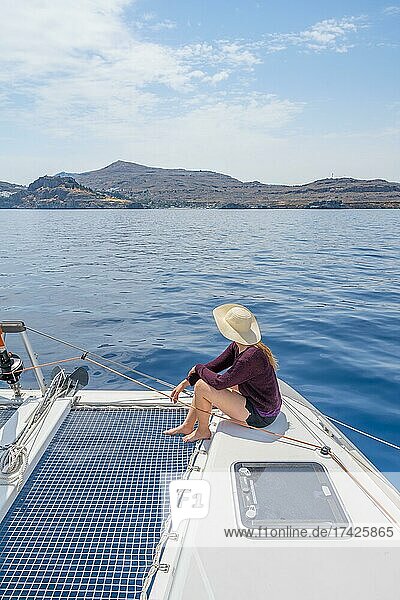 Young woman with hat sitting on deck at the net of a sailing catamaran  sailing trip  Rhodes  Dodecanese  Greece  Europe