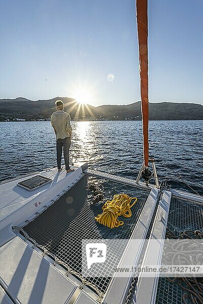 Junger Mann steht auf einem Katamaran und blickt in den Sonnenuntergang  Seile auf einem Segel-Katamaran  Sonnenstern  Segeltörn  Tilos  Dodekanes  Griechenland  Europa