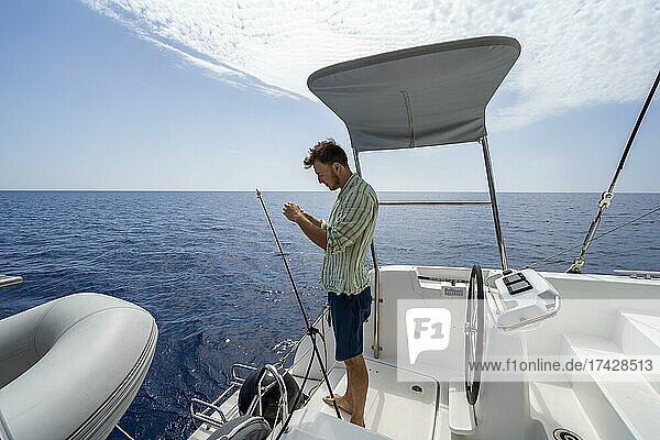 Young man fishing on a boat  sailing catamaran  sailing trip  Dodecanese  Greece  Europe