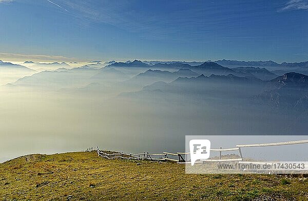 Meadow with fence and Lake Garda in the morning mist with Lake Garda mountains and Bergamo Alps  Monte Baldo  Malcesine  Verona Italy  Trentino-Alto Adige  Italy  Europe