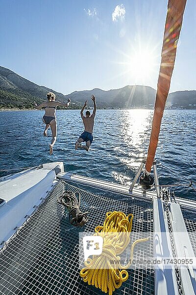 Young woman and young man jumping into the water  ropes on a sailing catamaran  Sun Star  sailing trip  Tilos  Dodecanese  Greece  Europe