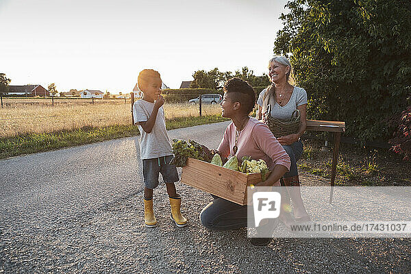 Lächelnde Mutter und Großmutter betrachten einen Jungen  der bei Sonnenuntergang Gemüse isst