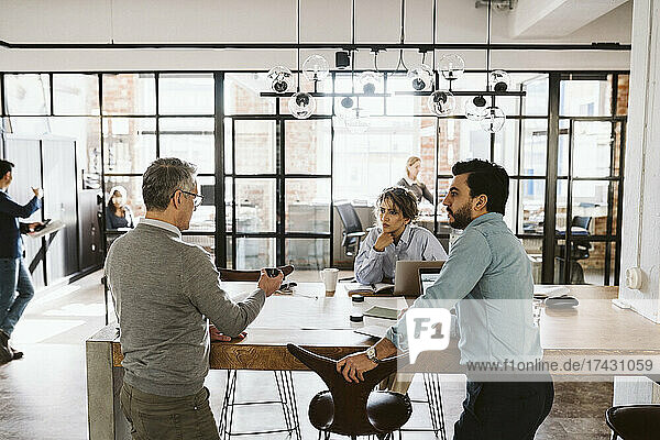 Male and female colleagues looking at mature businessman explaining in creative office