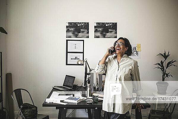 Ältere Handwerkerin lacht  während sie im Büro mit dem Handy telefoniert