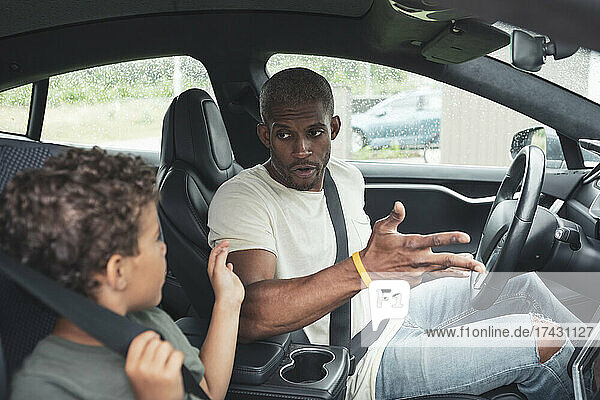 Junge im Gespräch mit seinem Vater  während er in einem Elektroauto sitzt