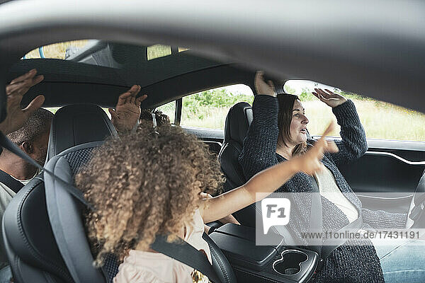 Glückliche Familie mit erhobenen Händen in einem Elektroauto sitzend