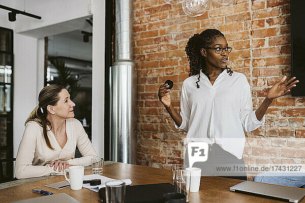 Eine Unternehmerin erklärt ein Produkt  während sie neben einer Geschäftsfrau im Sitzungssaal steht