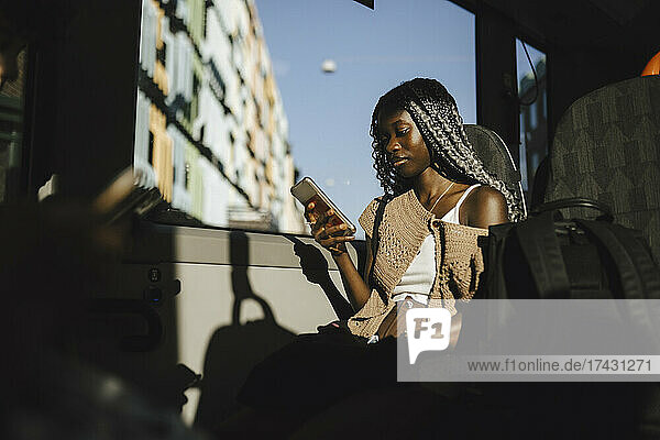 Junge Frau benutzt Smartphone im Bus an einem sonnigen Tag