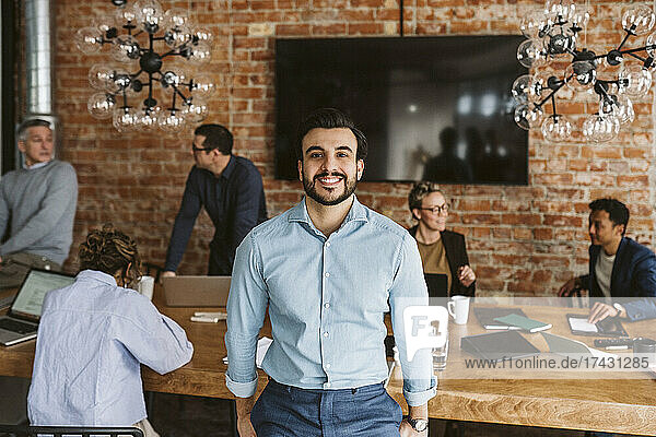 Porträt eines glücklichen männlichen Berufstätigen  während im Hintergrund Kollegen diskutieren