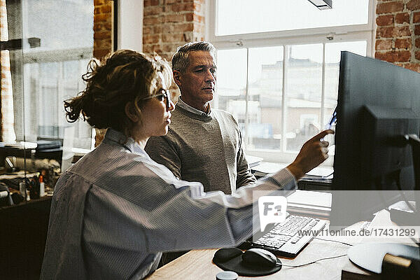 Female professional explaining businessman while pointing on computer in office