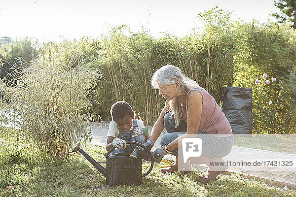 Boy and grandmother crouching with watering can at farm