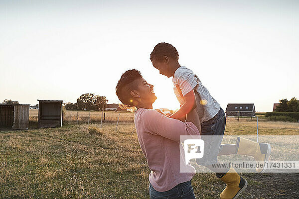 Fröhliche Mutter und Sohn spielen auf dem Bauernhof bei Sonnenuntergang