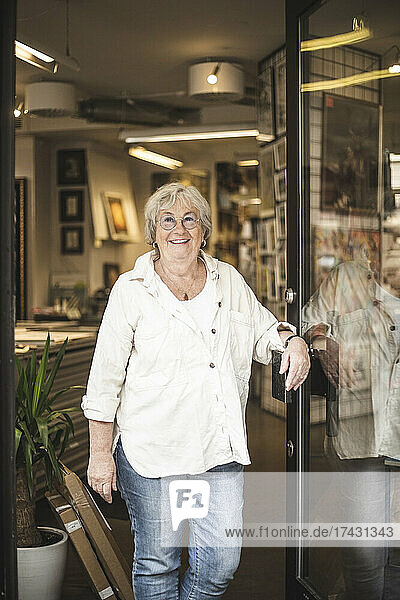 Smiling senior female owner standing by door at workshop