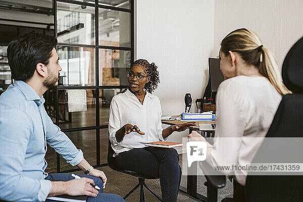 Eine Unternehmerin bespricht einen Plan  während sie mit Kollegen im Büro sitzt
