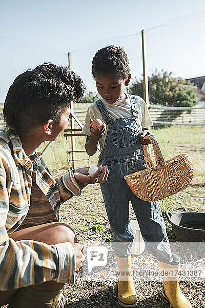 Junge  der ein Ei betrachtet  während er bei seiner Mutter auf dem Bauernhof steht  an einem sonnigen Tag