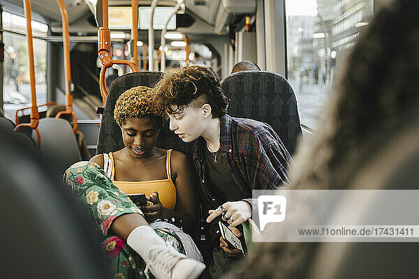 Jugendlicher schaut auf junge nicht-binäre Frau  die im Bus ein Smartphone benutzt