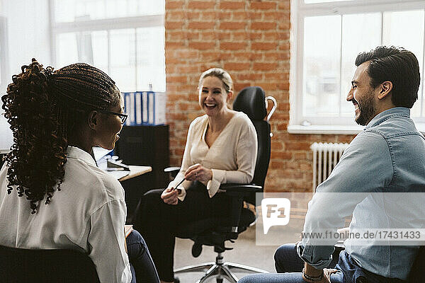 Female and male professionals laughing while discussing in office