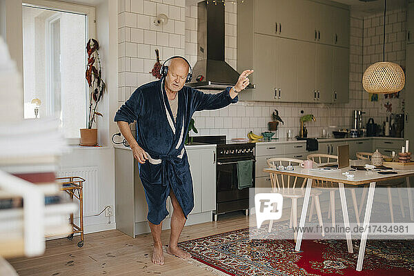 Älterer Mann tanzt  während er in der Küche über Kopfhörer Musik hört