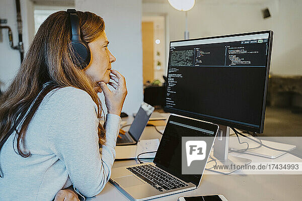 Mature female hacker brainstorming while coding over computer in office