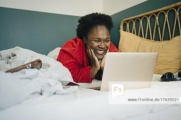 Lächelnde Frau  die zu Hause auf dem Bett liegend auf ihren Laptop schaut