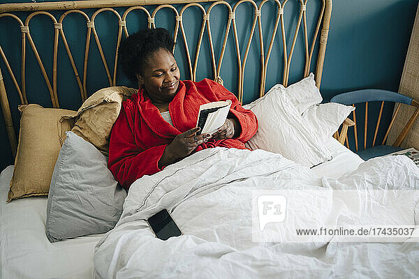 Lächelnde Frau liest ein Buch auf dem Bett zu Hause