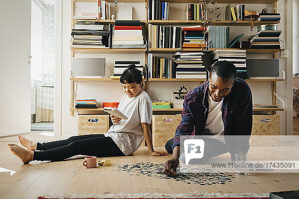 Mann spielt Puzzle  während seine Freundin im Wohnzimmer ein Buch liest