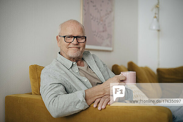 Porträt eines älteren Mannes mit Kaffeetasse  der zu Hause auf dem Sofa sitzt