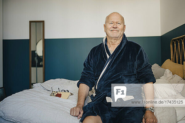 Porträt eines lächelnden älteren Mannes im Bademantel auf dem Bett zu Hause