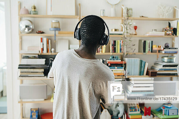 Rückansicht eines mittelgroßen erwachsenen Mannes  der zu Hause über Kopfhörer Musik hört