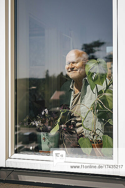 Lächelnder älterer Mann schaut durch ein Fenster an einem sonnigen Tag