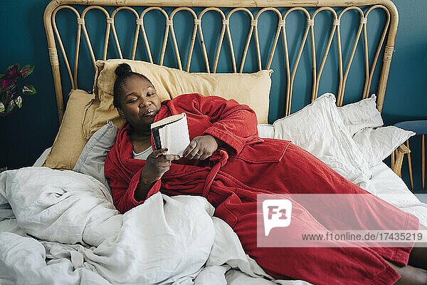 Mid adult woman reading book while relaxing on bed