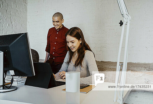 Lächelnder weiblicher Hacker mit Laptop bei der Arbeit mit Kollegen in einem Startup-Unternehmen