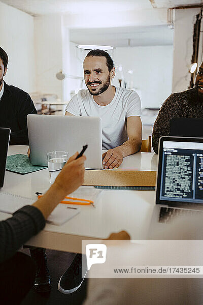 Lächelnder männlicher Hacker bei einem Geschäftstreffen mit Kollegen im Kreativbüro