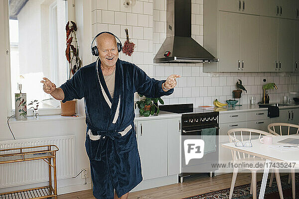 Fröhlicher älterer Mann mit Kopfhörern tanzt in der Küche zu Hause