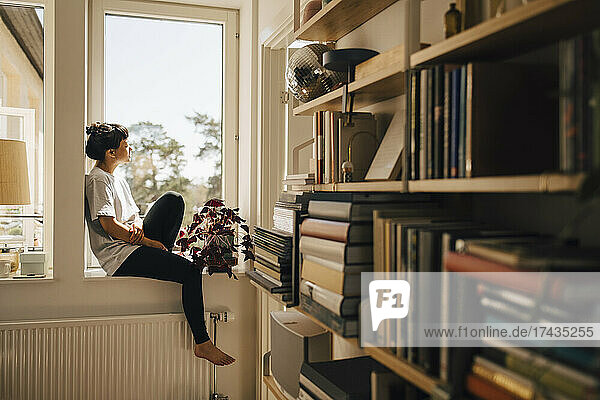 Frau sitzt auf Fensterbank im Sonnenlicht zu Hause