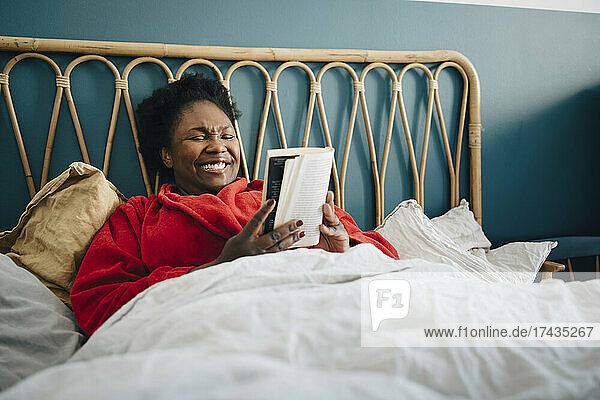 Lächelnde Frau liest ein Buch  während sie zu Hause auf dem Bett sitzt