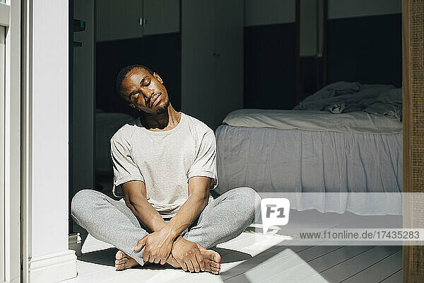 Mittlerer erwachsener Mann meditiert auf dem Boden sitzend im Schlafzimmer zu Hause