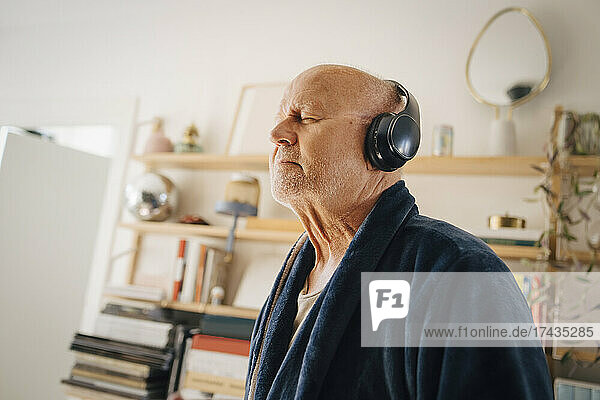 Senior man listening music with eyes closed through headphones at home