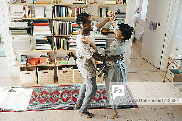 Lächelnde multirassische Paar tanzen zusammen im Wohnzimmer zu Hause