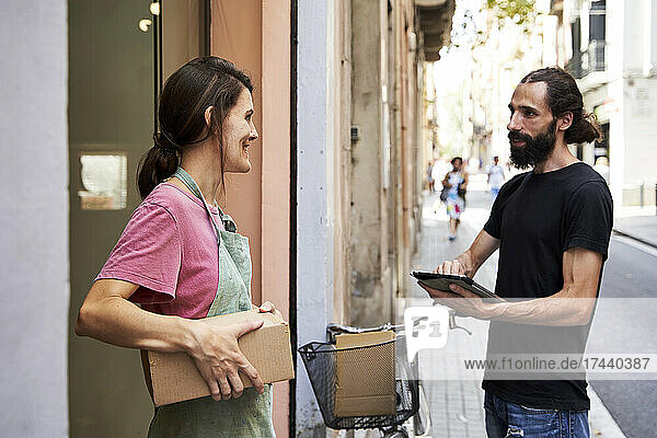 Male delivery person holding digital tablet talking with female entrepreneur outside store
