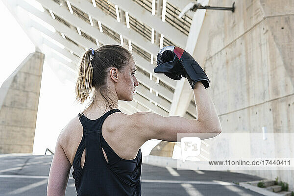 Serious female athlete flexing muscles while wearing boxing glove