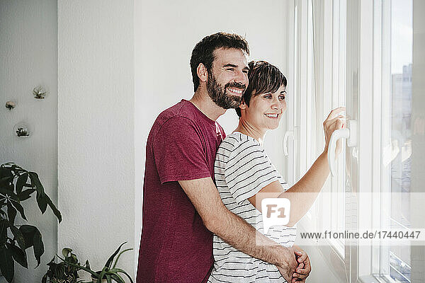 Man embracing woman while looking through window at home