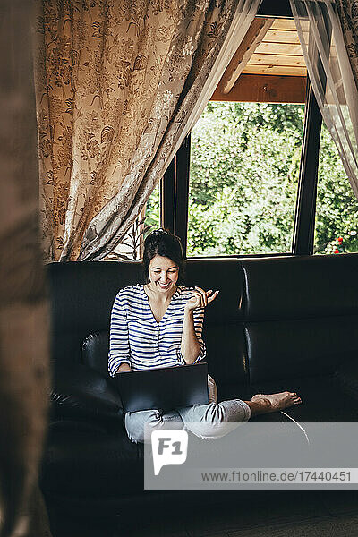 Lächelnde Frau gestikuliert während eines Videoanrufs über den Laptop zu Hause