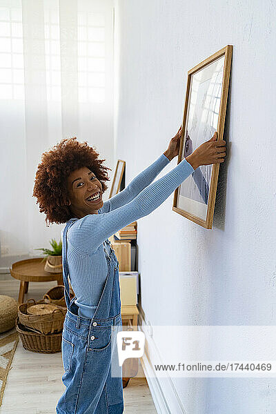 Happy woman adjusting picture frame on white wall
