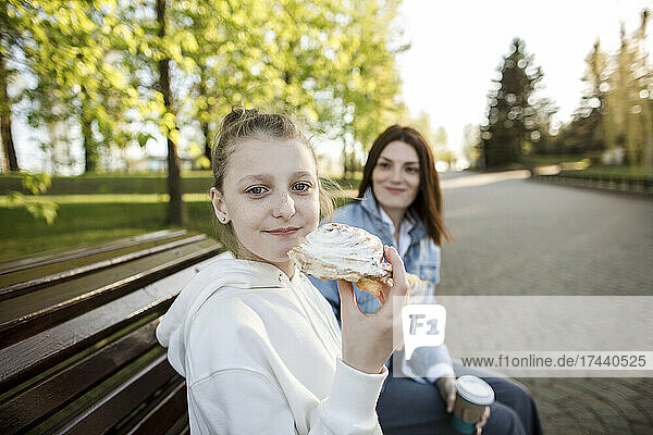 Girl having sweet food while sitting with mother on bench