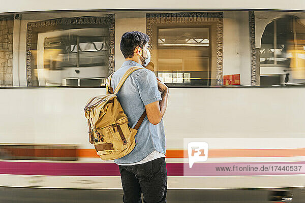 Mann mit Rucksack wartet am Bahnhof auf den Zug
