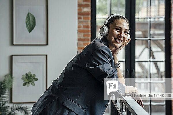 Happy female business professional with wireless headphones in office