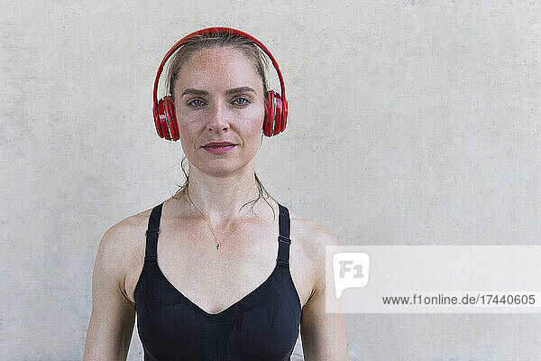 Sportswoman listening music through headphones in front of wall
